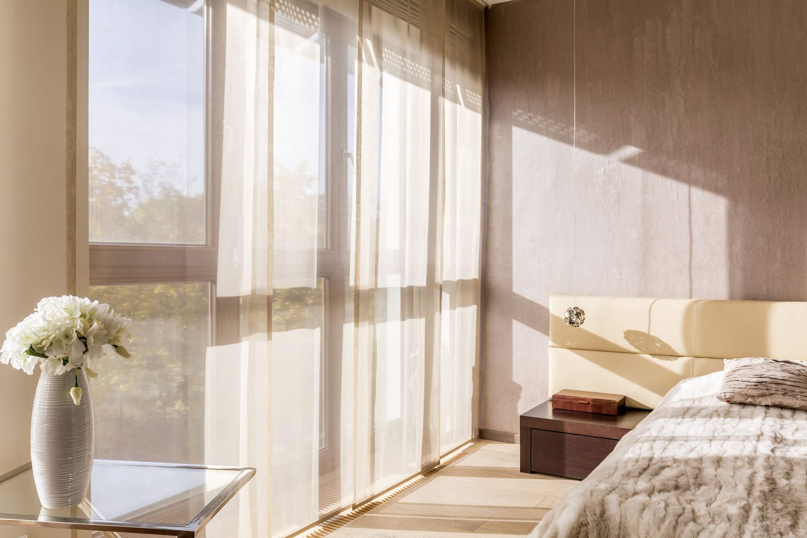 Die Sonne scheint durch weiße Gardinen in ein Schlafzimmer